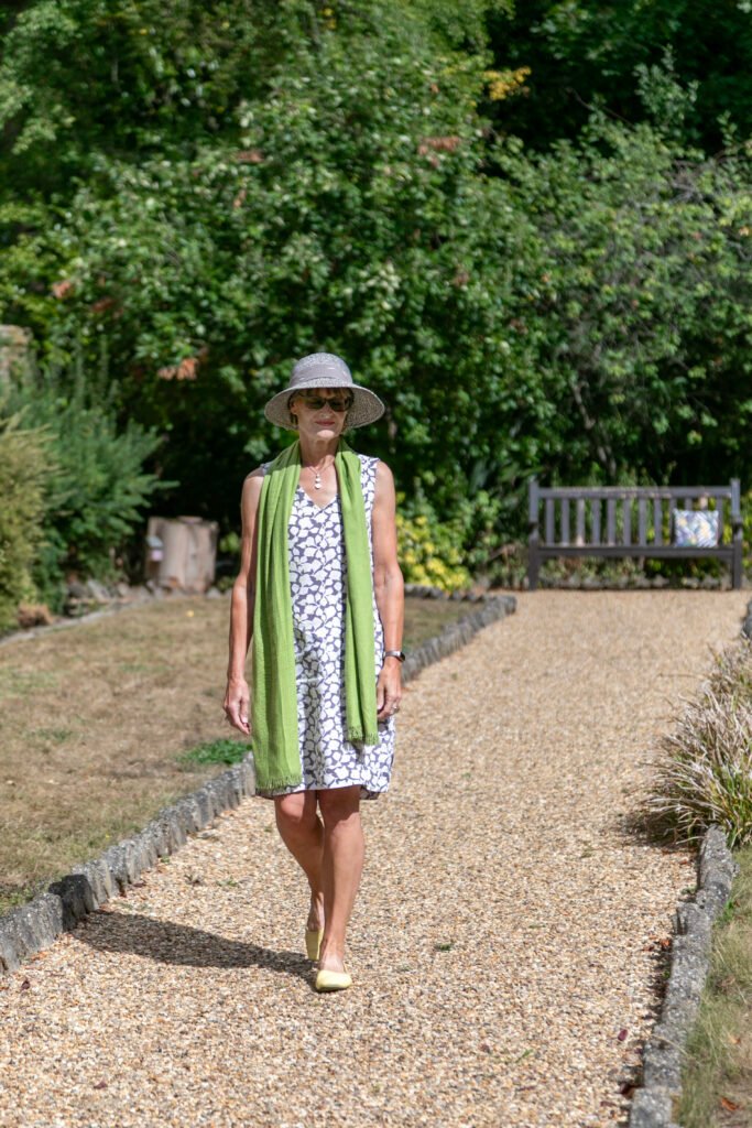 Linda in a wide brimmed hat walking along a gravel path in the sunshine